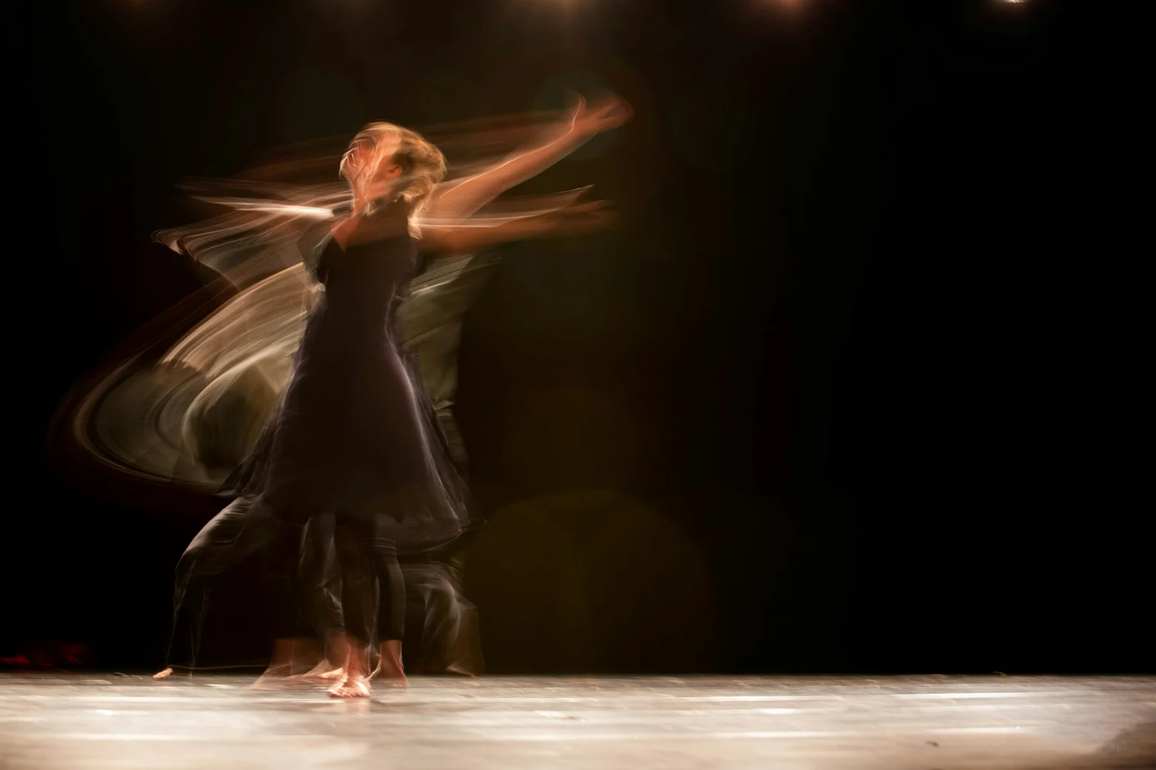 A dancer's blurred, sweeping turn on a dark stage, illustrative of Pina Bausch's Tanztheater style