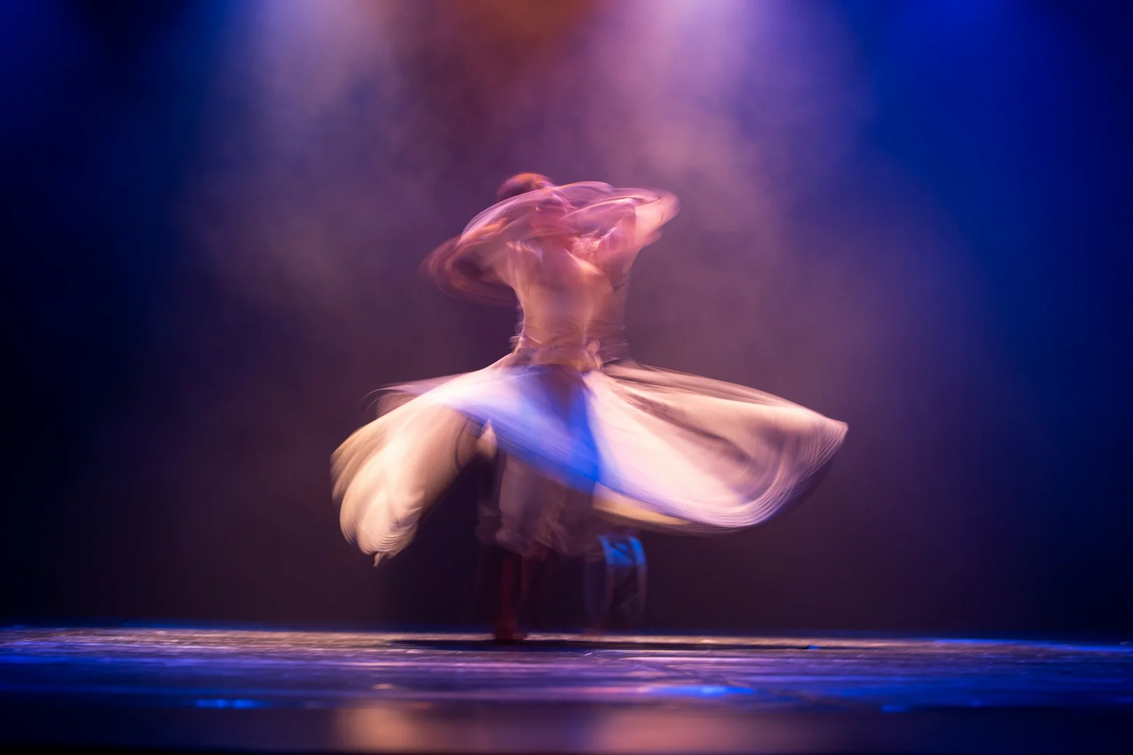 A dancer whirling in flowing robes under blue stage light, illustrative of Sidi Larbi Cherkaoui's cross-cultural, spiritually inflected choreography