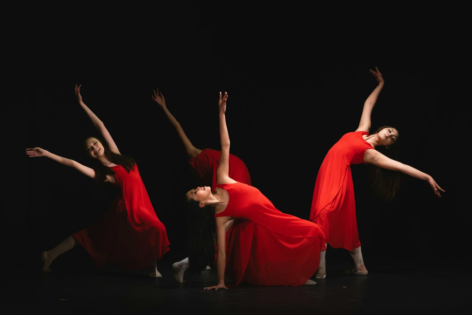Dancers in flowing red costumes caught in sharp, backlit poses against total darkness, illustrative of Grand Finale