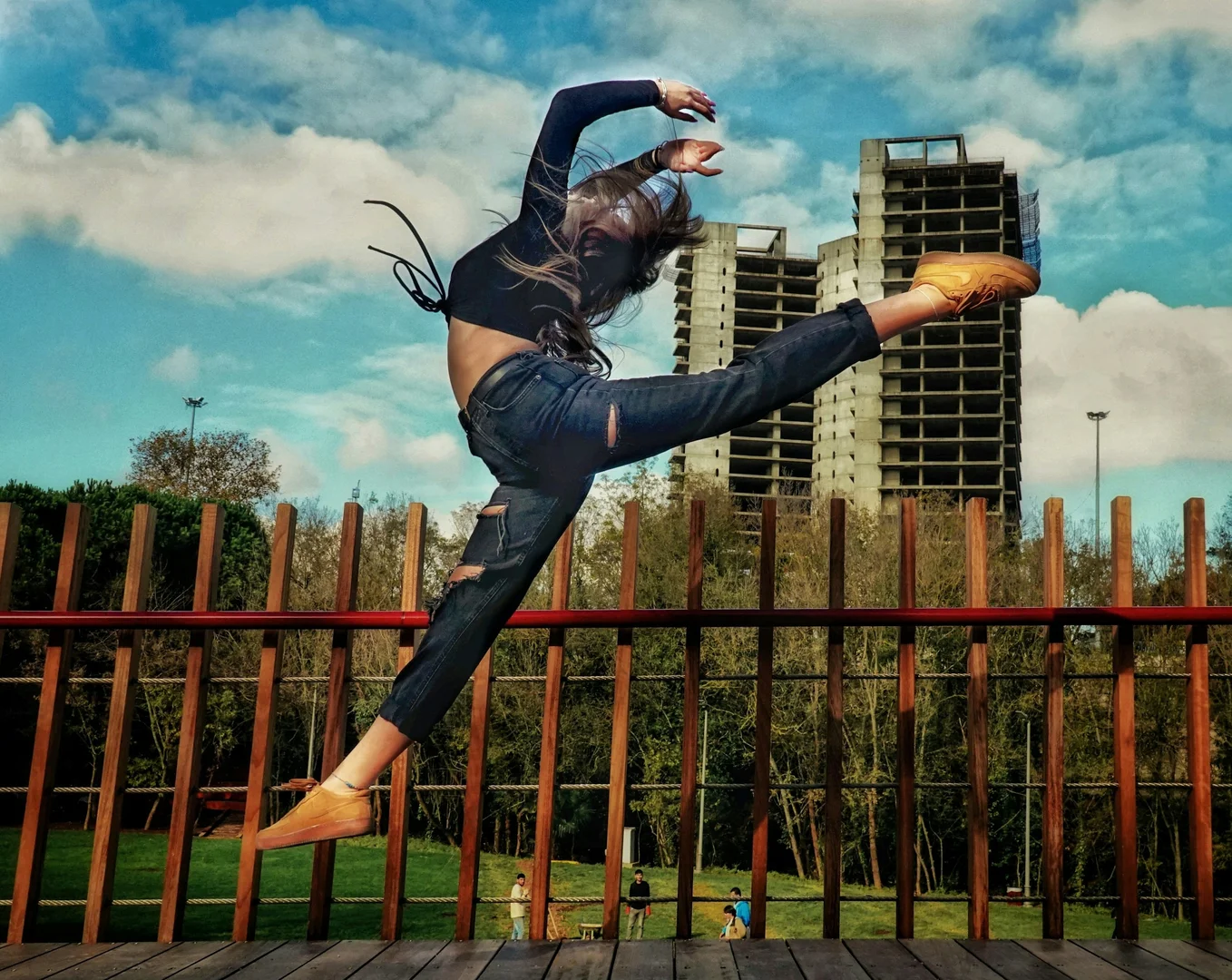 A dancer in mid-leap over a park railing against an urban skyline, illustrative of Justin Peck's restless, athletic choreographic energy