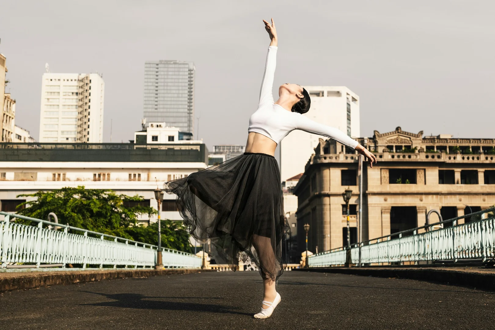 A dancer on pointe with a flowing skirt caught mid-turn against a city skyline, illustrative of Christopher Wheeldon's neoclassical narrative style
