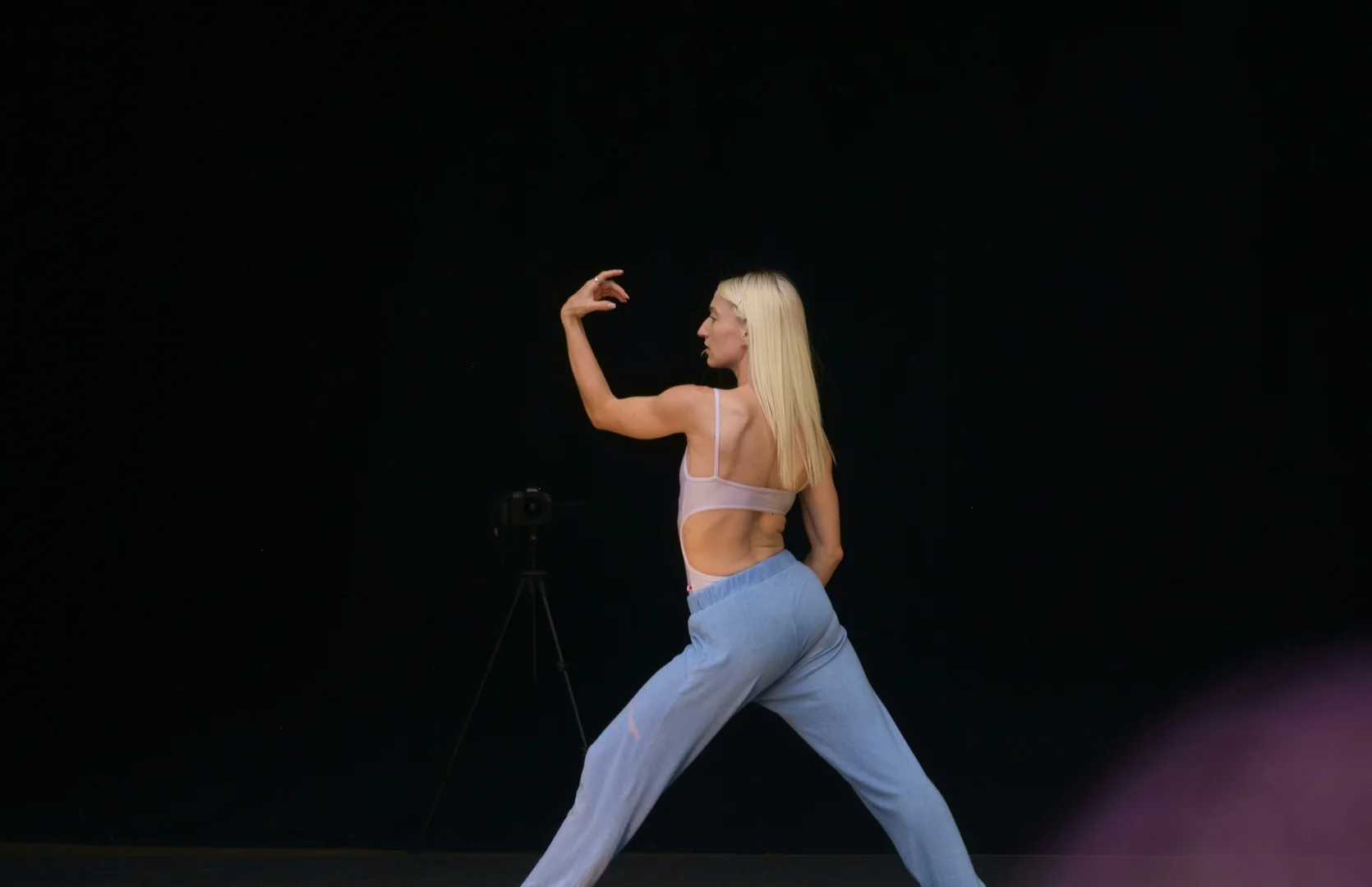 A dancer caught mid-gesture in a dynamic, off-center lean against a dark backdrop, illustrative of Kyle Abraham's house- and release-influenced choreographic style