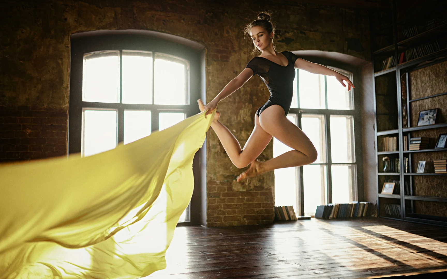 A dancer leaping through a sunlit, book-lined loft with fabric trailing behind her, illustrative of Cathy Marston's psychologically driven narrative style